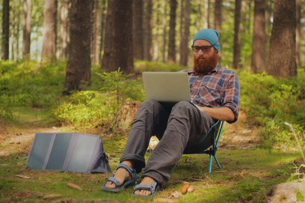Individual sat in the woods working on a laptop with a small tent to next to them