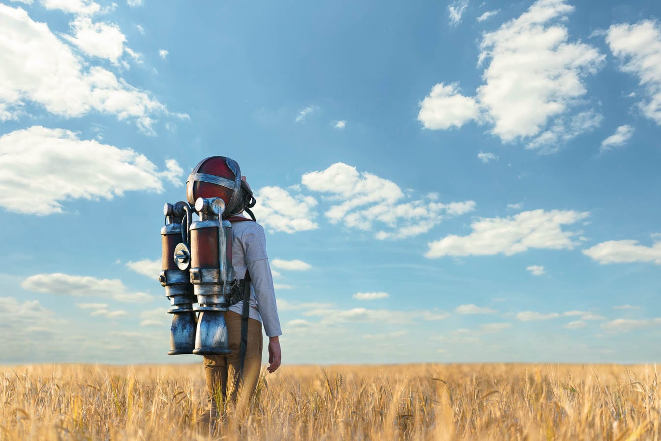 boy standing in wheat field wearing a jetpack